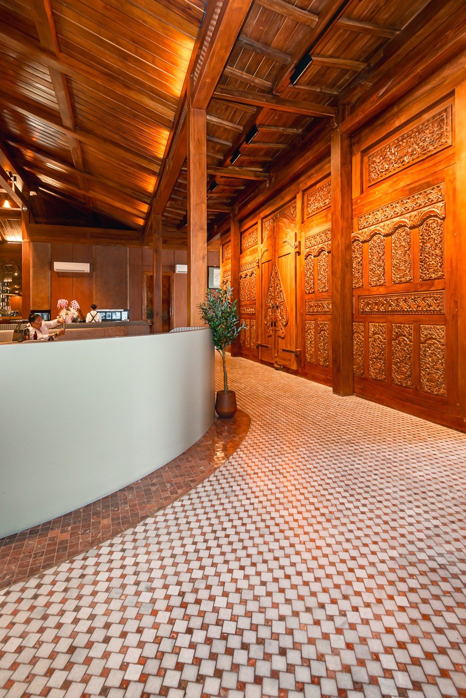 Elegant hotel lobby with intricate wood carvings and curved reception desk under a wooden ceiling.