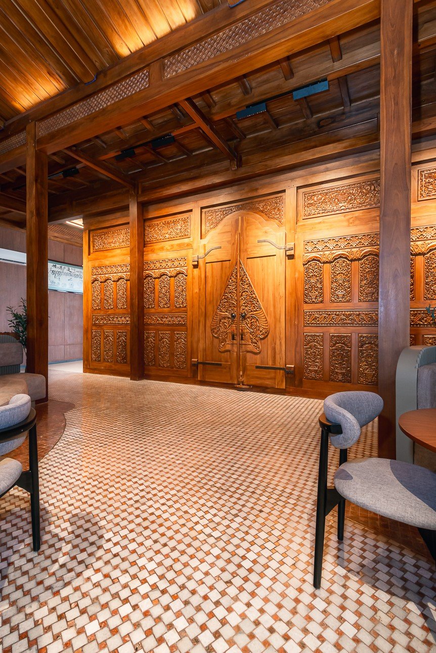 Elegant wooden interior with intricate carvings on door, checkered floor, and modern seating furniture.