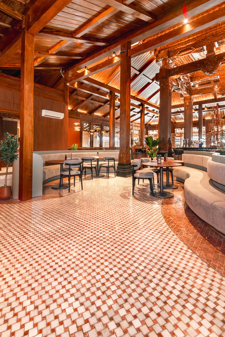 Spacious restaurant interior with elegant wooden decor, marble tiled floor, and cozy seating arrangement.