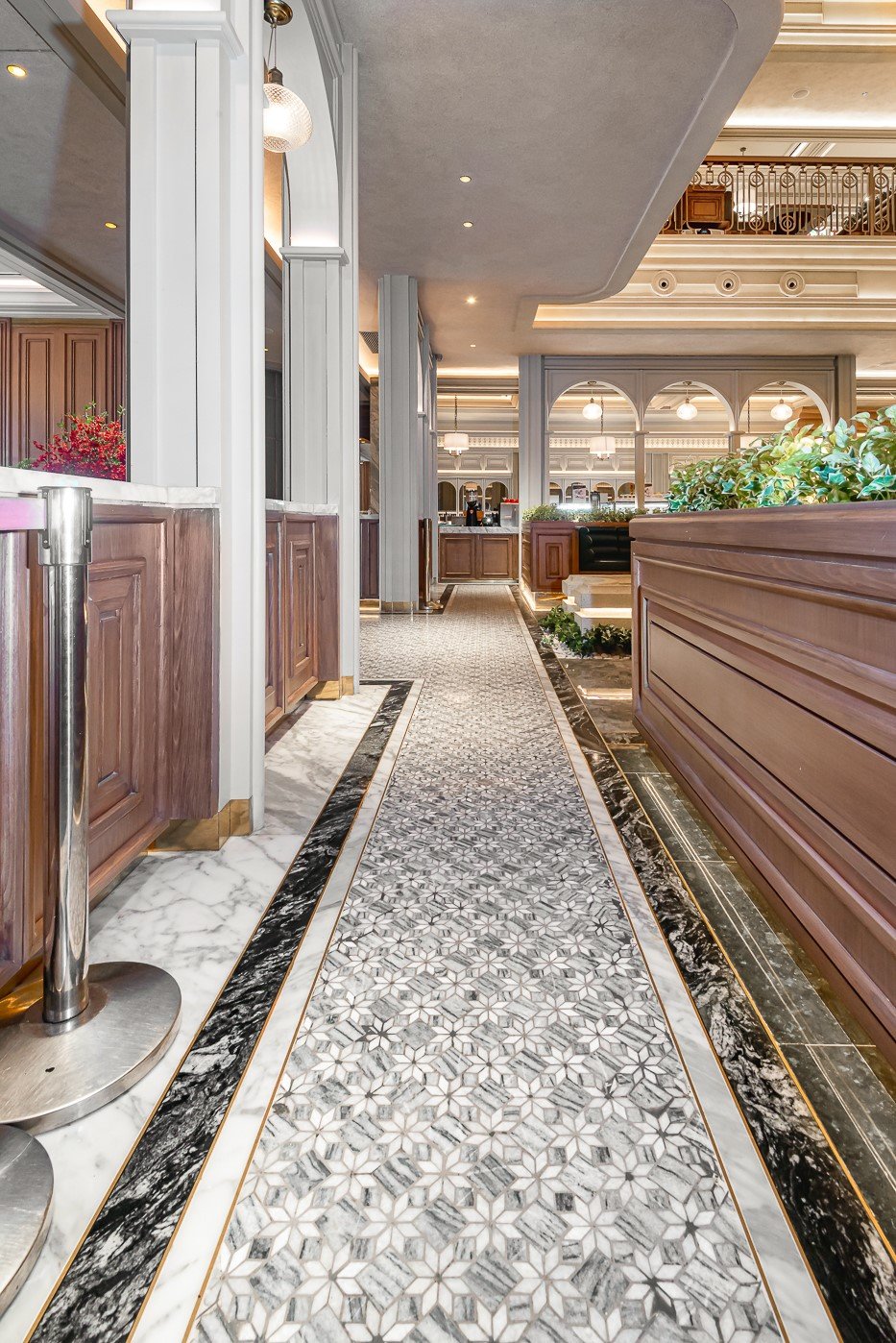 Elegant hotel lobby with intricate tile flooring, classic wood paneling, and lush green plants in modern design.