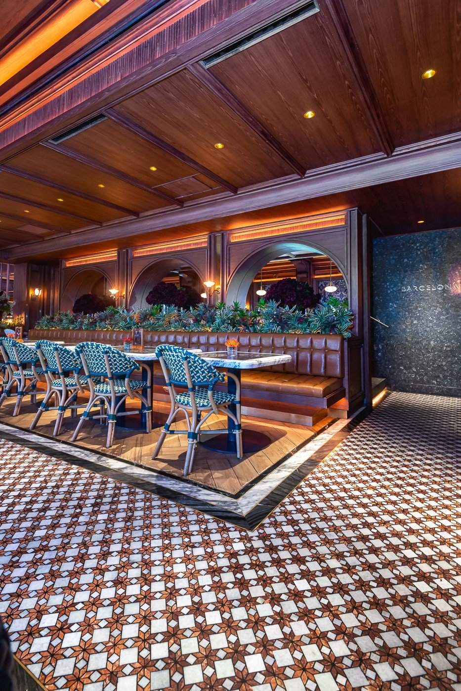 Elegant restaurant interior with patterned tile floor, leather seating, and chic chairs. Warm lighting complements the decor.