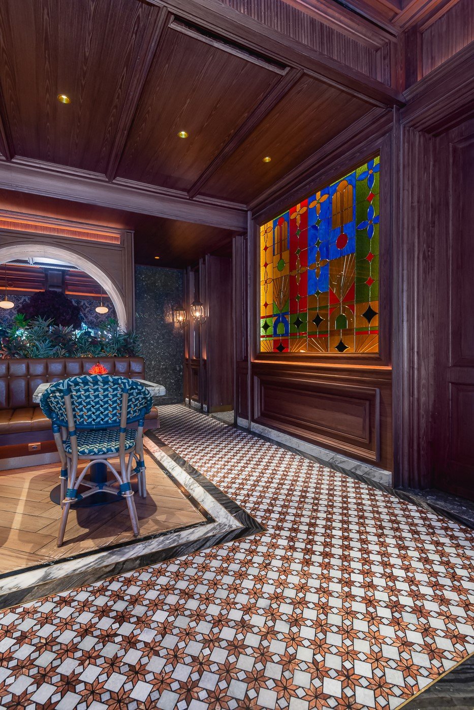 Stylish restaurant interior with stained glass, patterned floor tiles, and cozy seating under warm lighting.