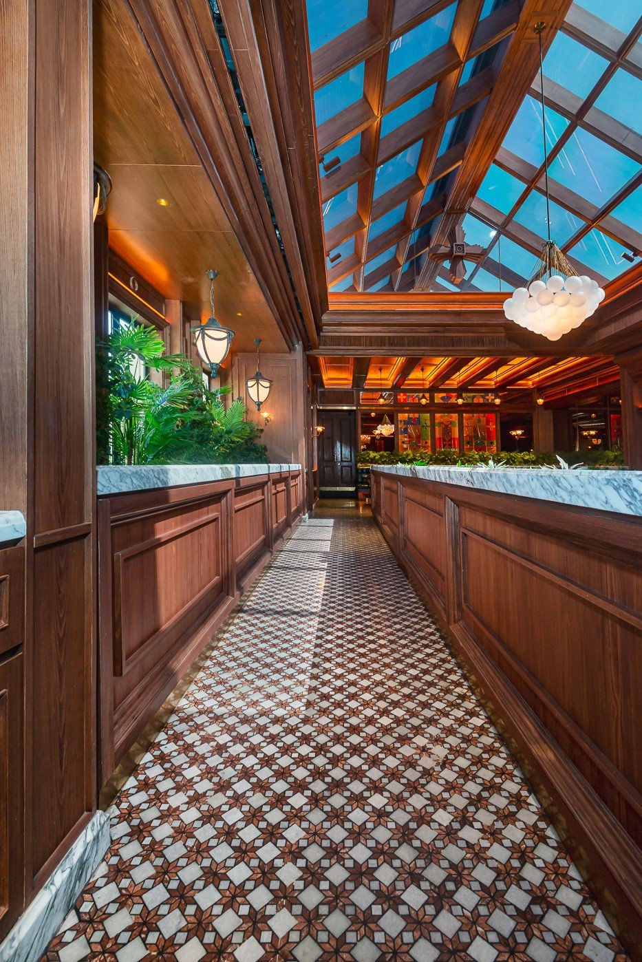 Luxurious restaurant interior with elegant wooden decor, patterned floor tiles, and a stunning glass ceiling.